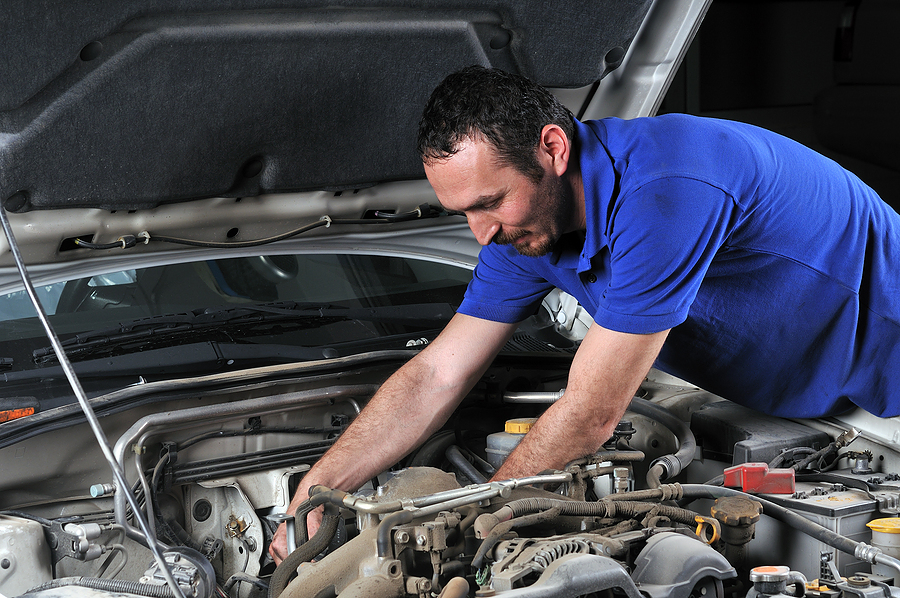 Automotive technician working beneath an open hood